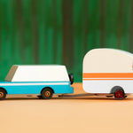 Candylab Toys Rosebud Toy Camper hitched to a teal wooden wagon against a green forest backdrop