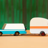 Candylab Toys Rosebud Toy Camper hitched to a teal wooden wagon against a green forest backdrop