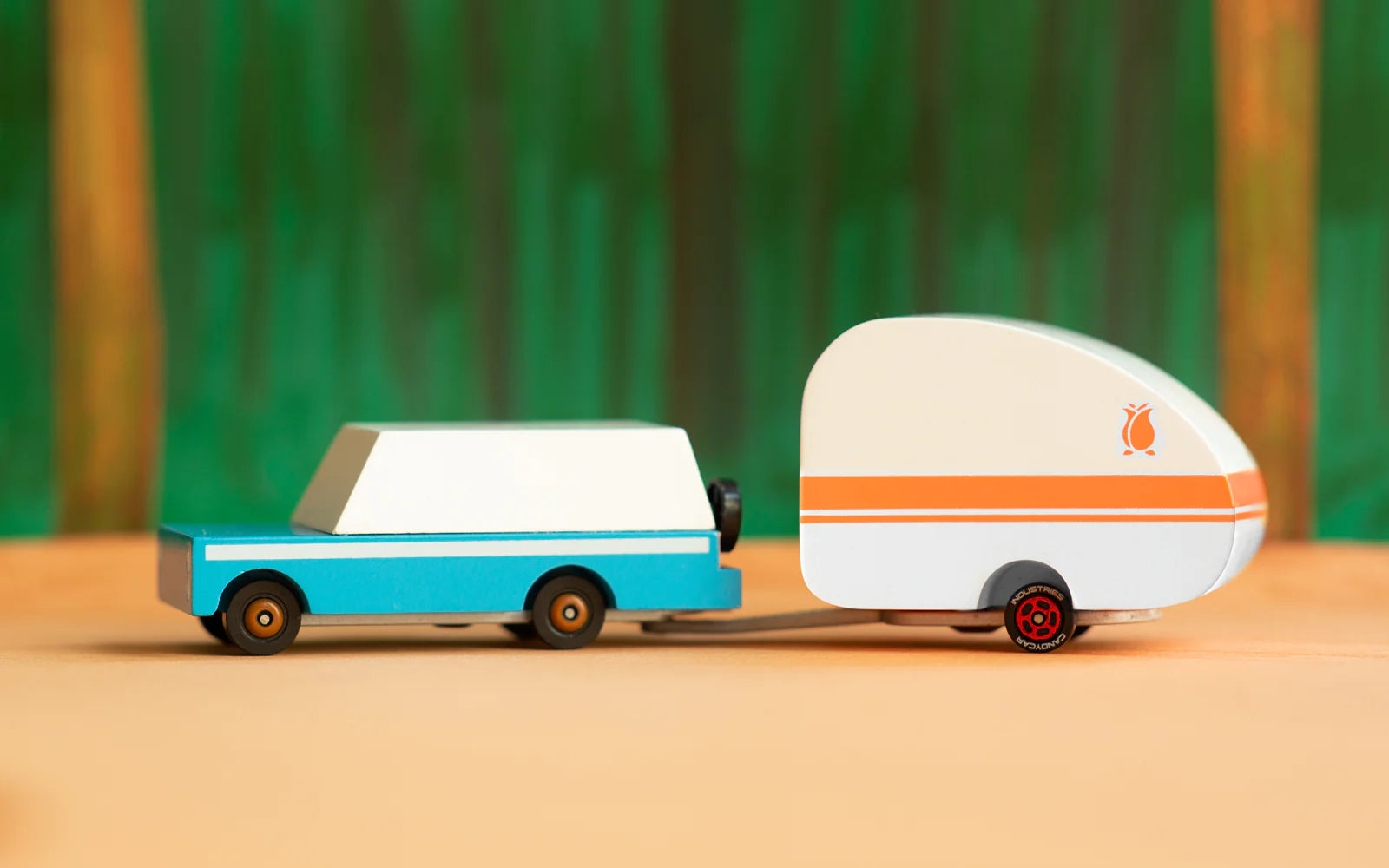 Candylab Toys Rosebud Toy Camper hitched to a teal wooden wagon against a green forest backdrop