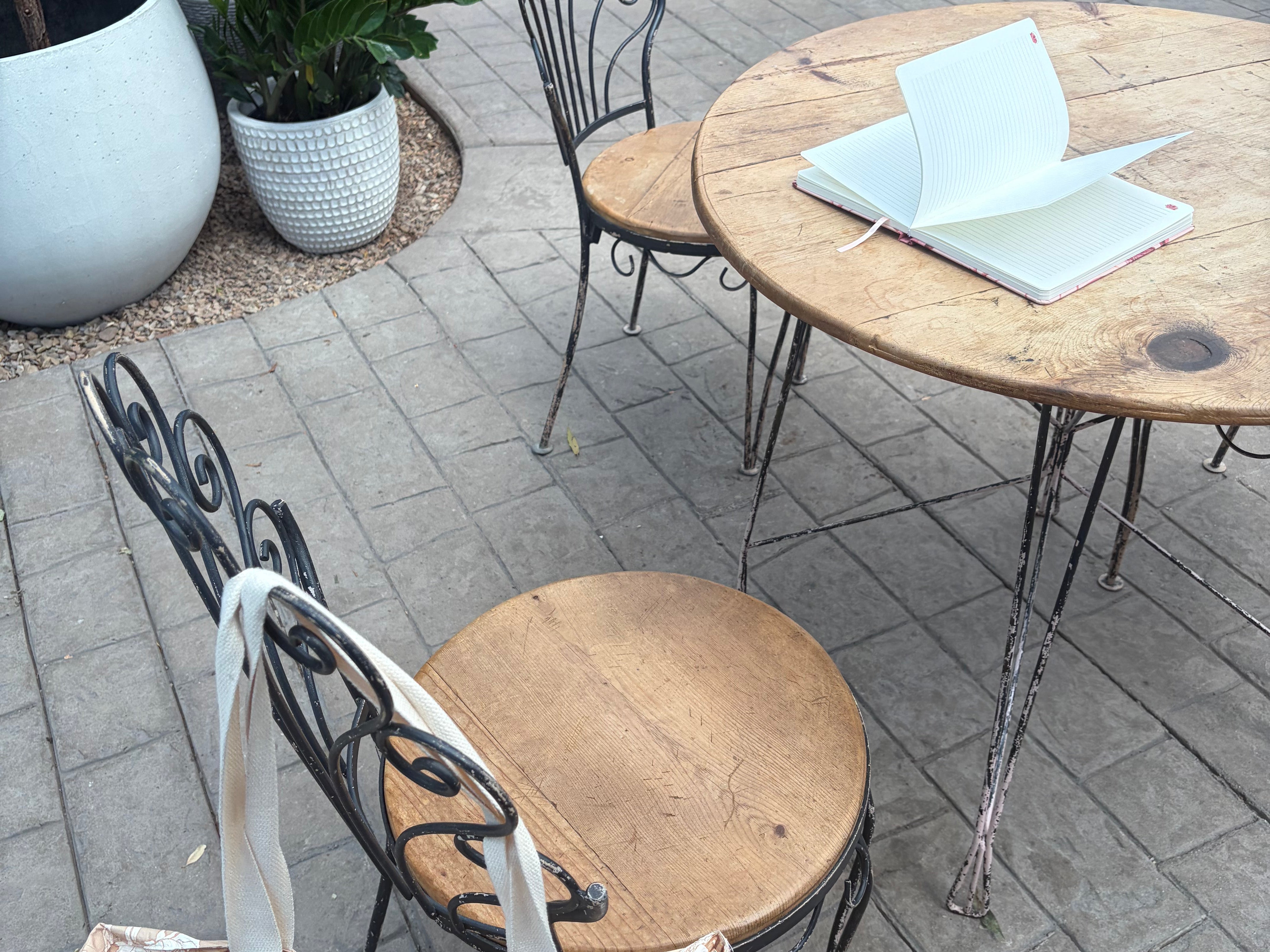 The Canyon Rose tote leaning against a bistro chair on a greenhouse patio, with an open notebook on the table.