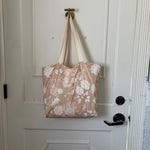 The Canyon Rose tote hanging from a hook on a white panelled door, warm clay rose printed with white roses and daisies.