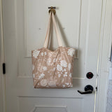The Canyon Rose tote hanging from a hook on a white panelled door, warm clay rose printed with white roses and daisies.