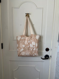 The Canyon Rose tote hanging from a hook on a white panelled door, warm clay rose printed with white roses and daisies.
