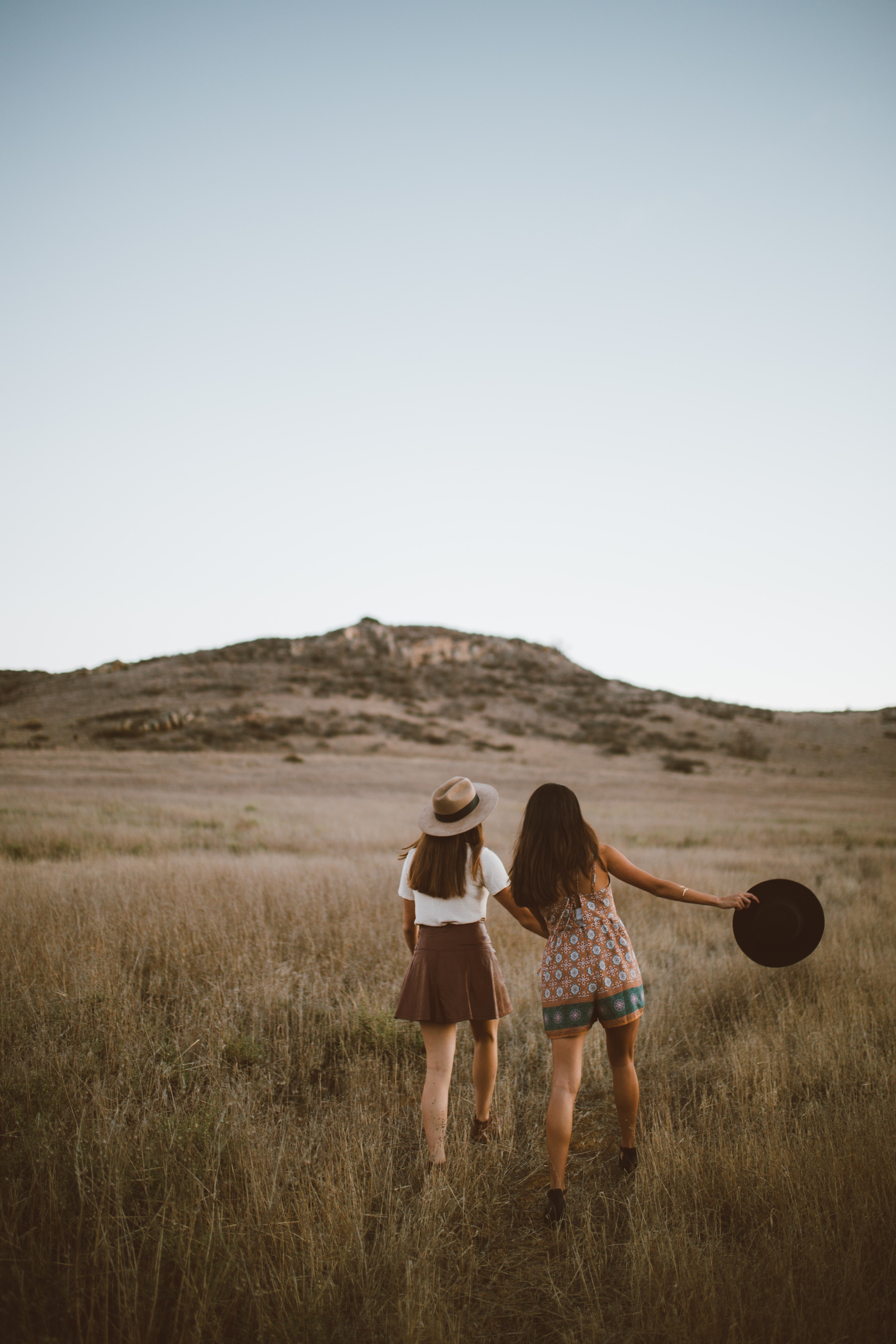 Two young women in grassy western field in wide brim hats and dresses
