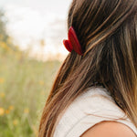 The Garnet Classic claw clip in deep red holding a half up section of long brown hair.