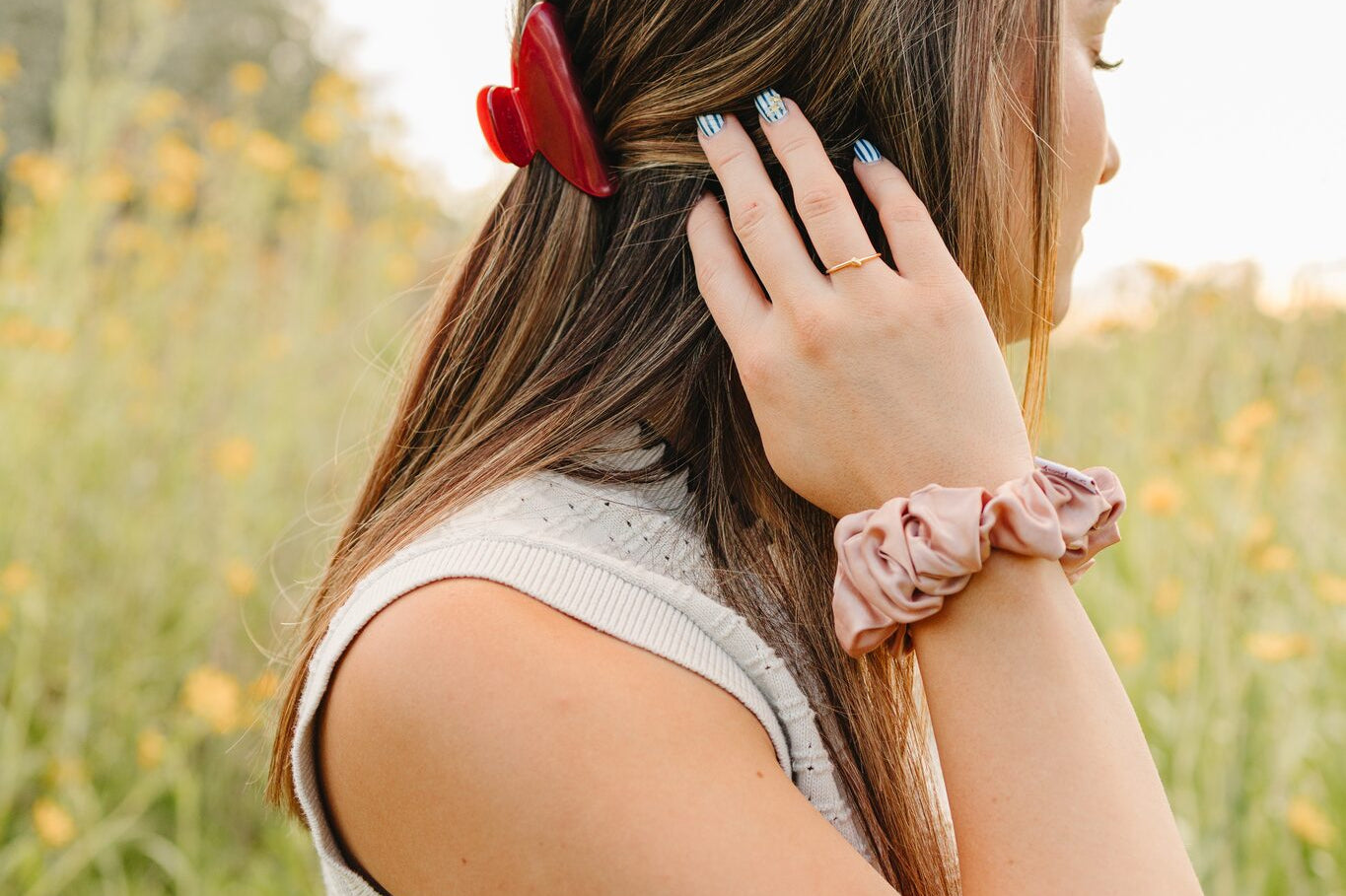 The Garnet Classic claw clip worn with a blush silk scrunchie on the wrist, in a field at golden hour.