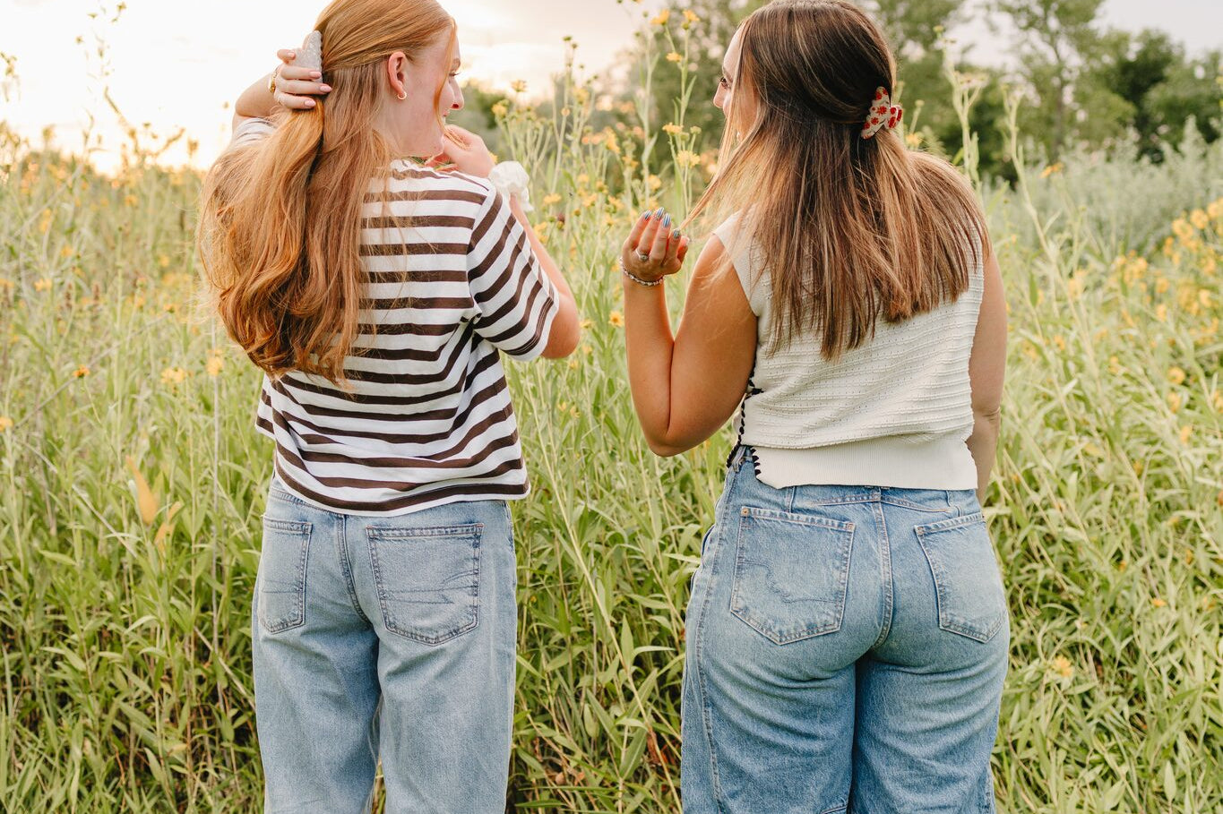 Two women standing in tall grass at sunset, each wearing a Classic claw clip in a half up style.