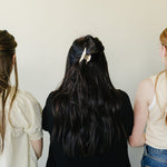 Three women photographed from behind, each wearing a Classic Claw Clip in dusty blue, marbled cream, and a floral print.