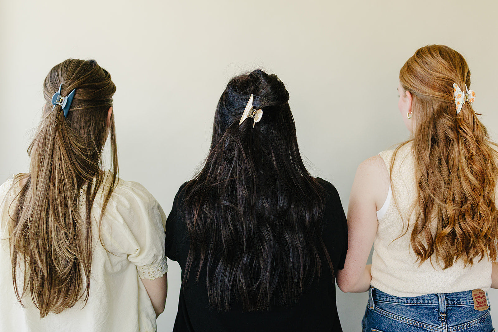 Three women photographed from behind, each wearing a Classic Claw Clip in dusty blue, marbled cream, and a floral print.
