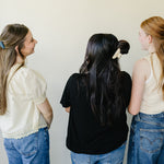 Three women in jeans with their backs turned, wearing Classic Claw Clips in dusty blue and marbled cream.