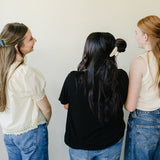Three women in jeans with their backs turned, wearing Classic Claw Clips in dusty blue and marbled cream.