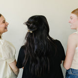 Three women laughing together, wearing Classic Claw Clips in dusty blue, marbled cream, and a floral print.