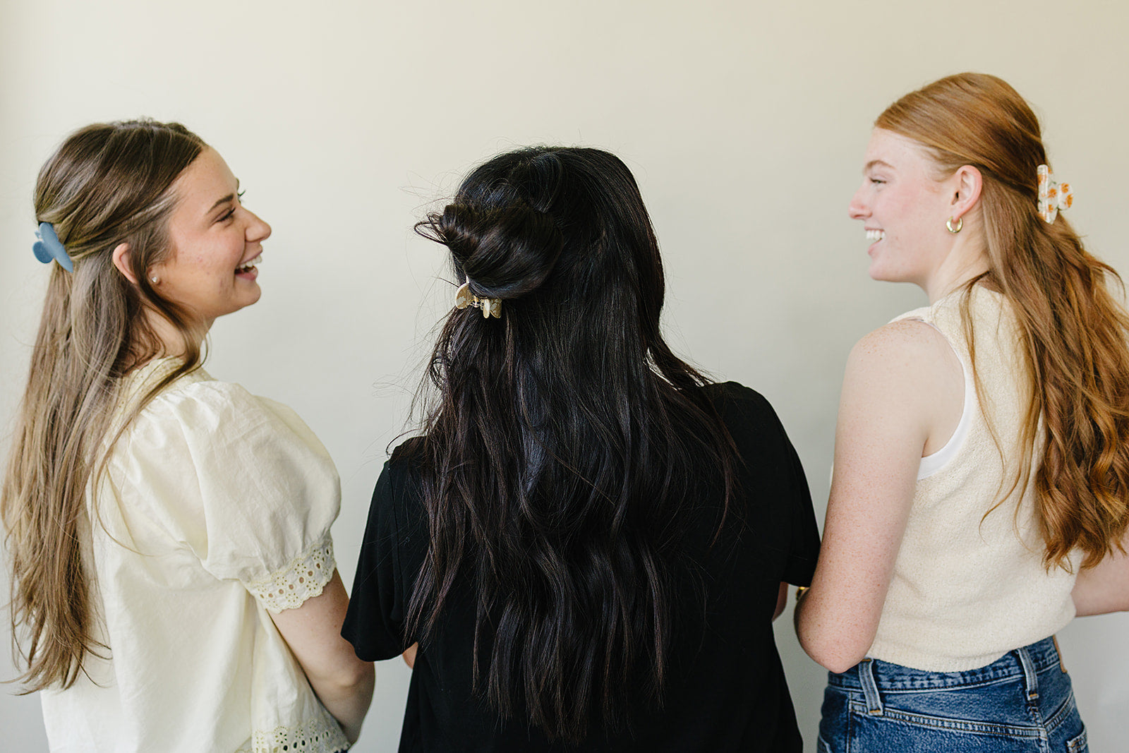 Three women laughing together, wearing Classic Claw Clips in dusty blue, marbled cream, and a floral print.