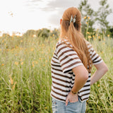 A woman in a wildflower field wearing a soft sage Classic claw clip in a half up style.