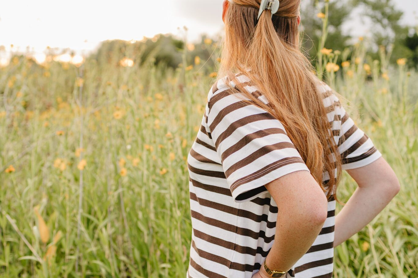 A woman in a wildflower field wearing a soft sage Classic claw clip in a half up style.