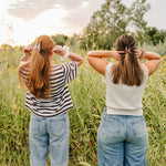 Two women seen from behind lifting their hair into Classic claw clips, with silk scrunchies on their wrists.