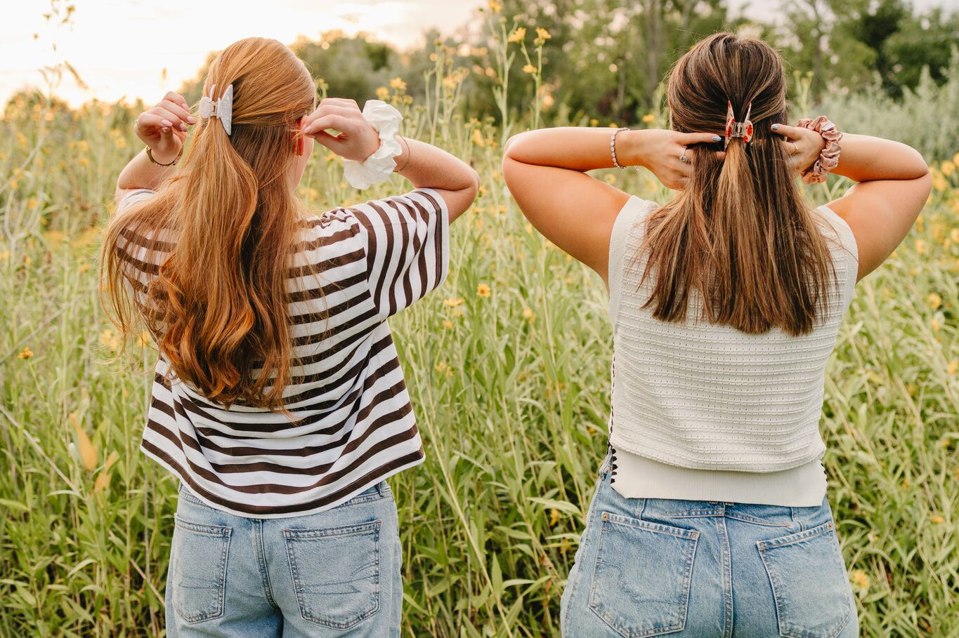 Two women seen from behind lifting their hair into Classic claw clips, with silk scrunchies on their wrists.