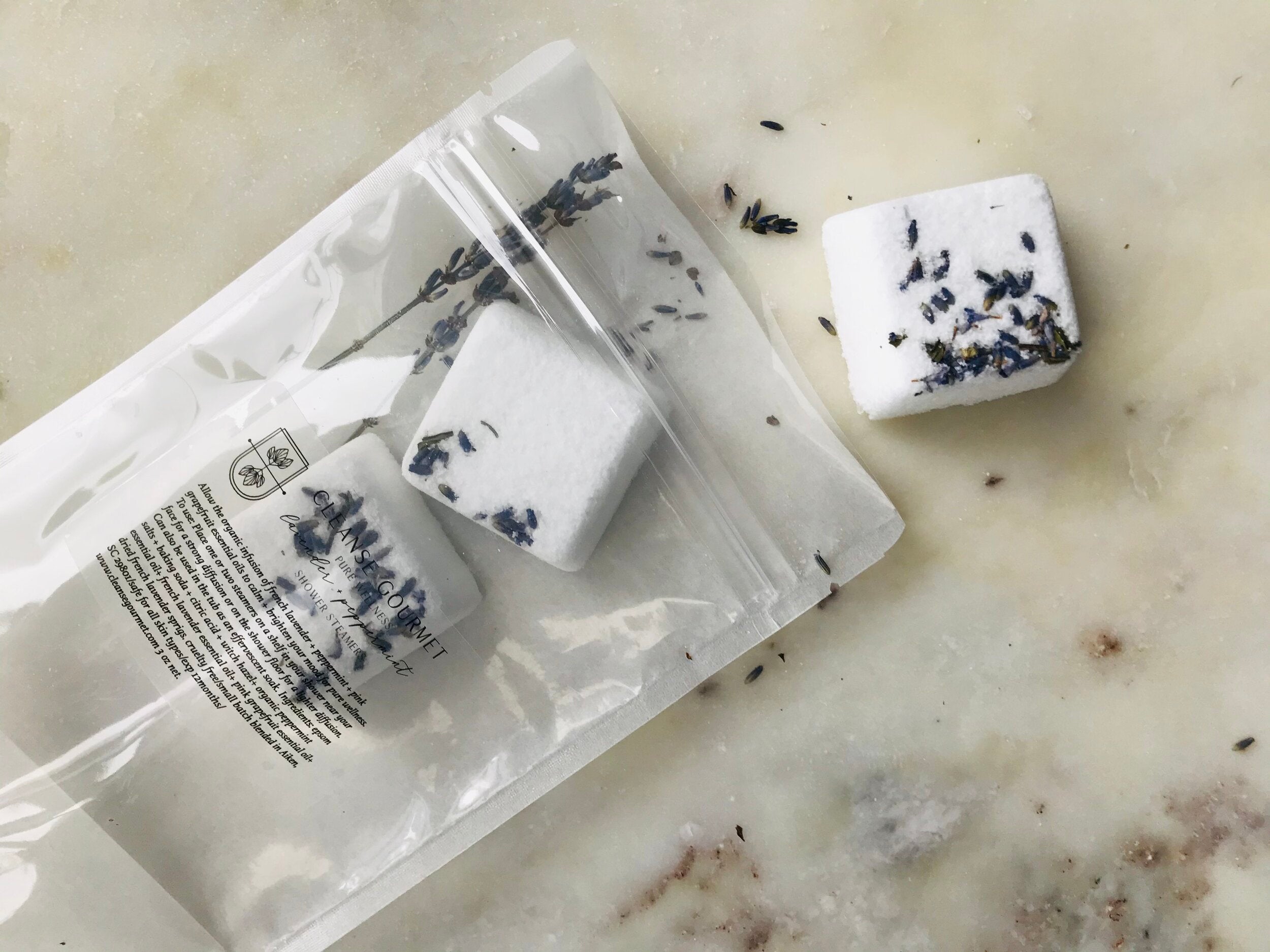 Cleanse Gourmet Pure Wellness Lavender + Peppermint Shower Steamers, white cubes with lavender buds in a clear pouch