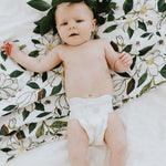 Baby lying on the Clementine Kids Magnolia Swaddle Blanket spread on a bed