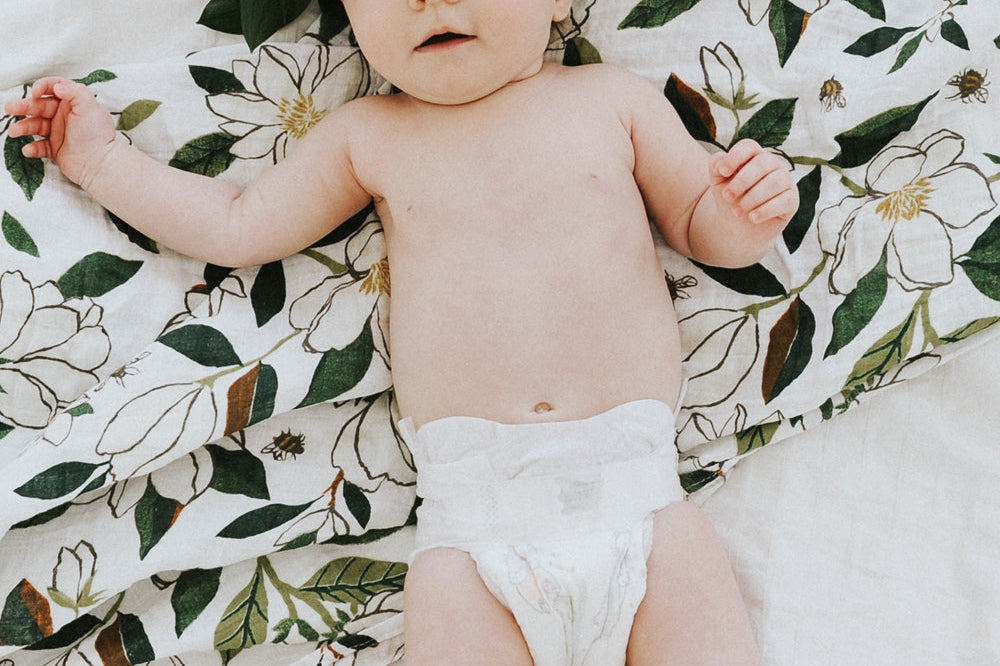 Baby lying on the Clementine Kids Magnolia Swaddle Blanket spread on a bed