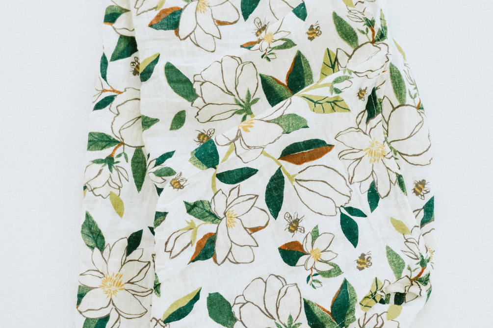 Clementine Kids Magnolia Swaddle Blanket, a white muslin swaddle with a green and white magnolia print, close-up