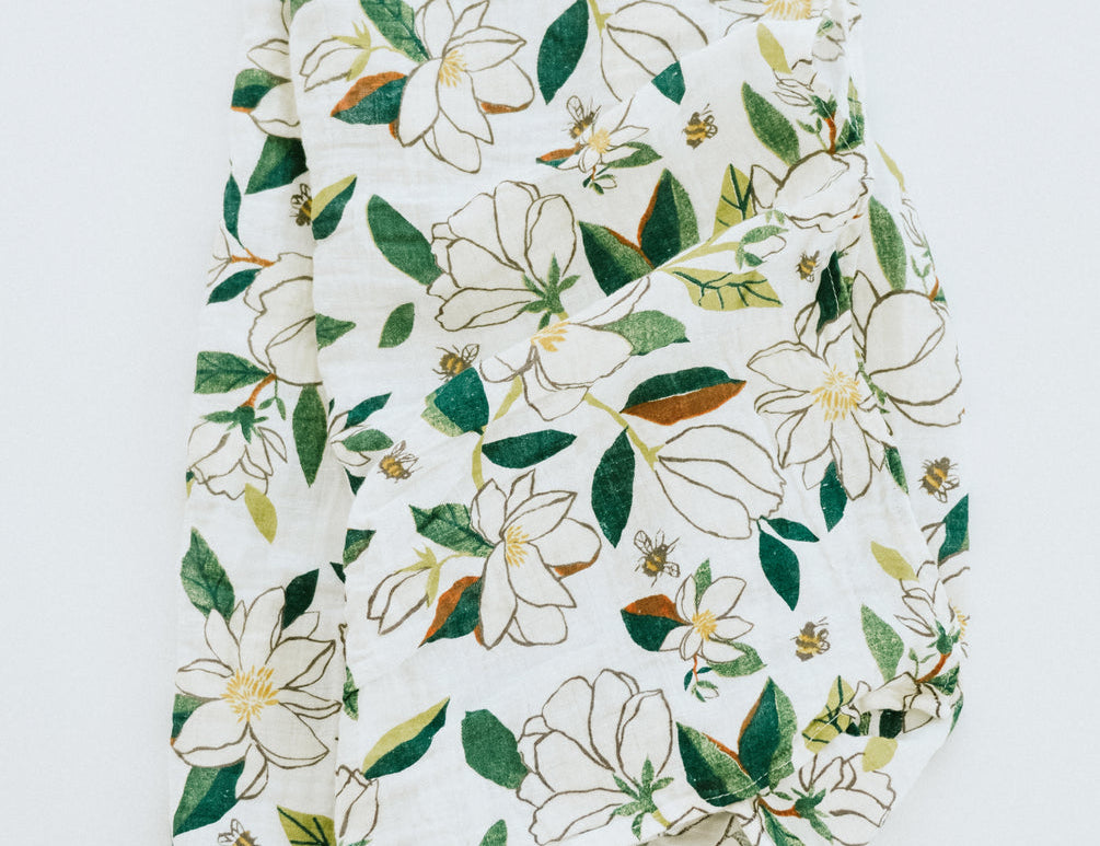 Clementine Kids Magnolia Swaddle Blanket, a white muslin swaddle with a green and white magnolia print, close-up