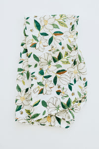 Clementine Kids Magnolia Swaddle Blanket, a white muslin swaddle with a green and white magnolia print, close-up