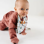Baby in a rust outfit crawling while wearing the Clementine Kids National Park Bib
