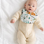 Baby in a cream knit outfit lying down wearing the Clementine Kids National Park Bib