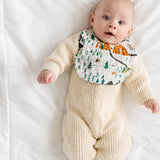 Baby in a cream knit outfit lying down wearing the Clementine Kids National Park Bib