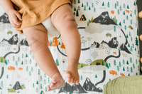 Baby in a mustard romper lying on the Clementine Kids National Parks Crib Sheet