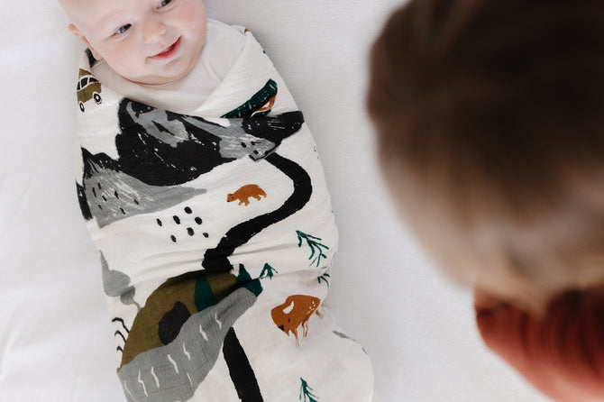 Smiling baby swaddled in the Clementine Kids National Parks Swaddle