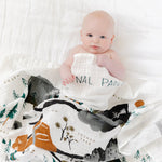 Baby wrapped in the Clementine Kids National Parks Swaddle on a white bed