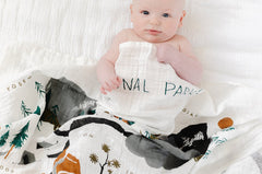 Baby wrapped in the Clementine Kids National Parks Swaddle on a white bed