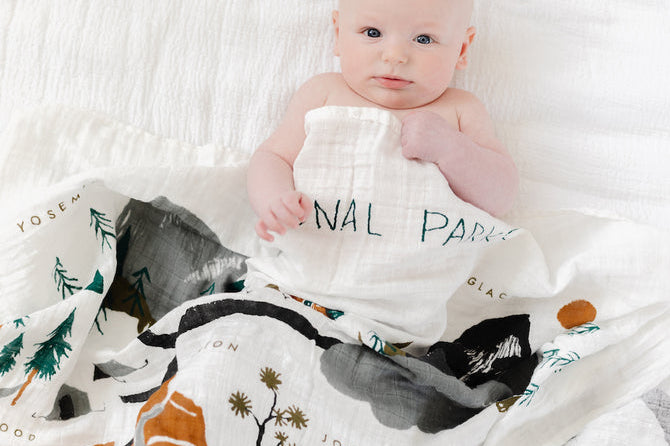 Baby wrapped in the Clementine Kids National Parks Swaddle on a white bed