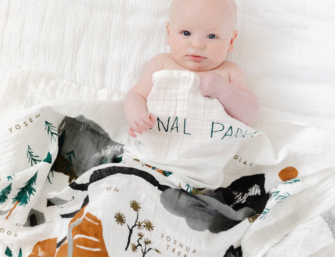 Baby wrapped in the Clementine Kids National Parks Swaddle on a white bed