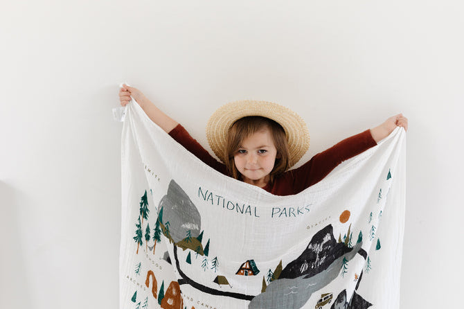 Child in a sun hat holding up the Clementine Kids National Parks Swaddle