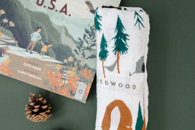 Clementine Kids National Parks Swaddle folded beside a National Parks of the USA book and pinecones