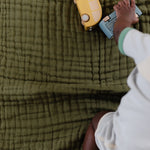 Baby playing with a toy on the olive green side of the Clementine Kids Reversible National Parks Quilt