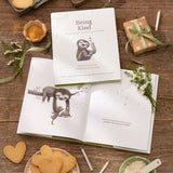 Compendium Being Kind book and open pages on a wooden table with heart-shaped cookies and small gifts