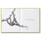 Compendium Being Kind book open to a page of a sloth hanging from a branch holding a flower