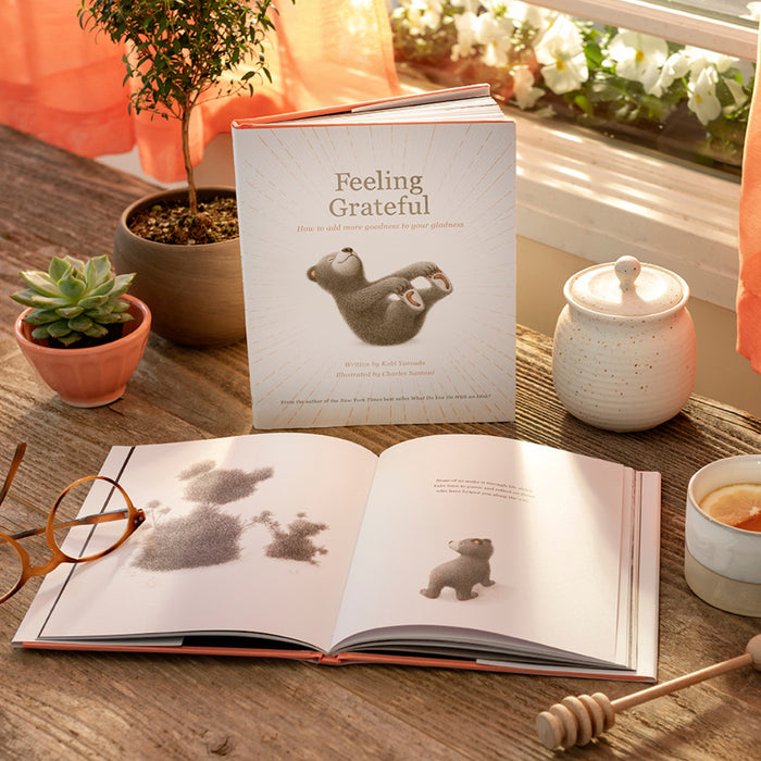 Compendium Feeling Grateful book on a wooden table with an open copy, plants and honey