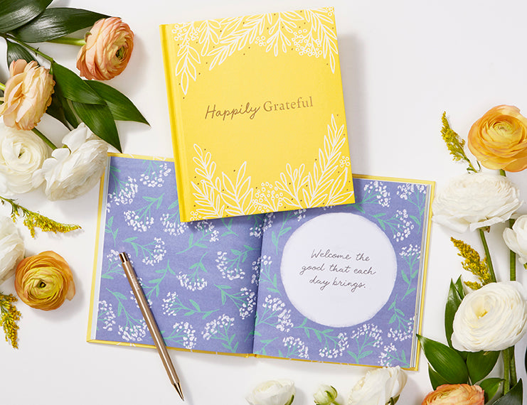 Compendium Happily Grateful book open to a purple floral page beside a closed copy and fresh flowers