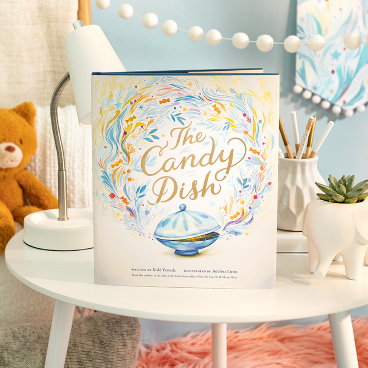 Compendium The Candy Dish book on a white nightstand with a teddy bear and lamp