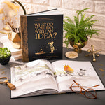 What Do You Do With an Idea? 10th Anniversary Edition book by Compendium, black and gold cover standing open on a desk with a fern and reading glasses