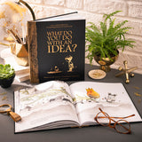 What Do You Do With an Idea? 10th Anniversary Edition book by Compendium, black and gold cover standing open on a desk with a fern and reading glasses