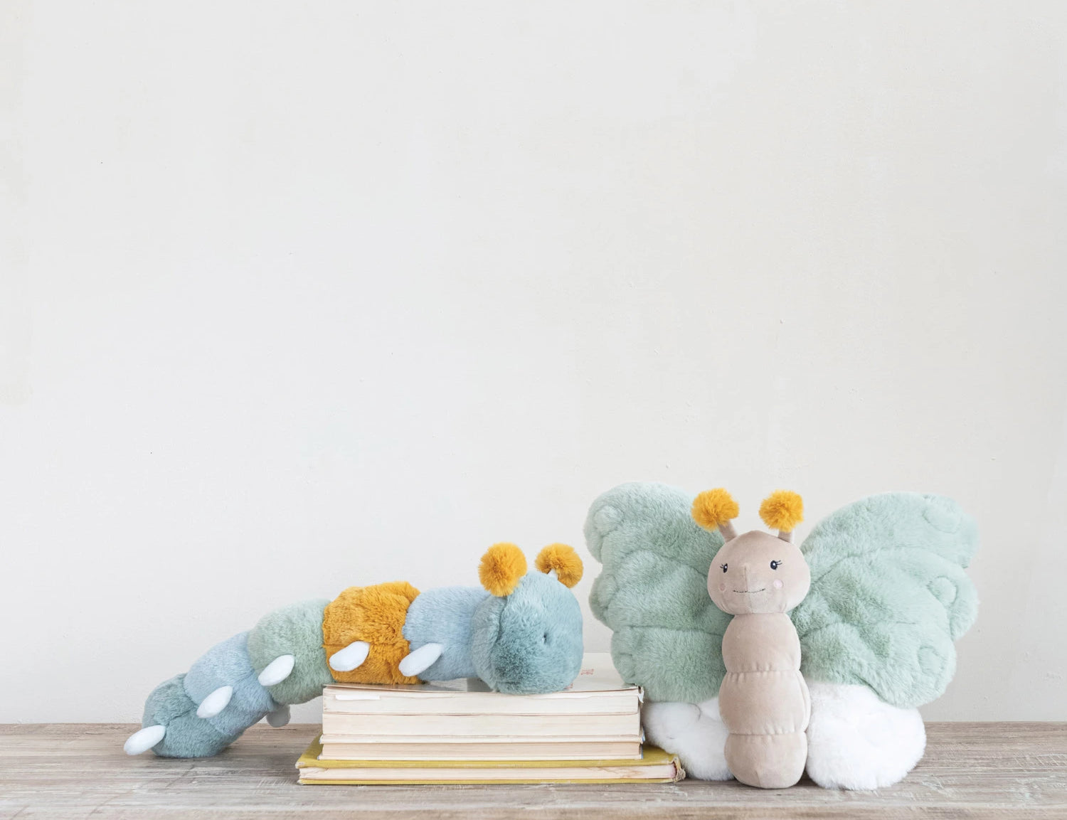 Creative Co-Op Butterfly Plush toys in sage, blue and mint stacked on books on a wood floor
