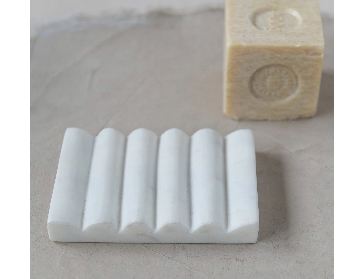Creative Co-Op Carved Marble Soap Dish with a bar of soap on a stone surface