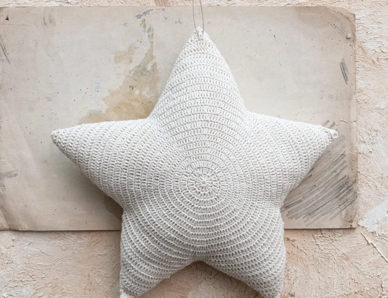 Creative Co-Op Cotton Crocheted Star Pillow, a cream crocheted star-shaped pillow on a stone surface