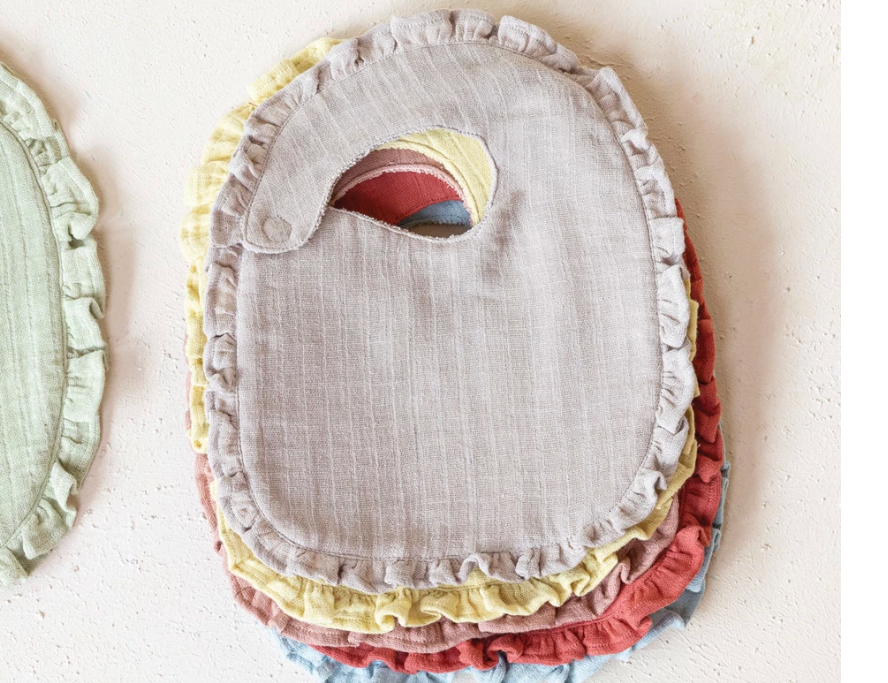 Creative Co-Op Cotton Double Cloth Baby Bibs stacked, with ruffled edges in tan, sage, yellow and rust and a toucan patch